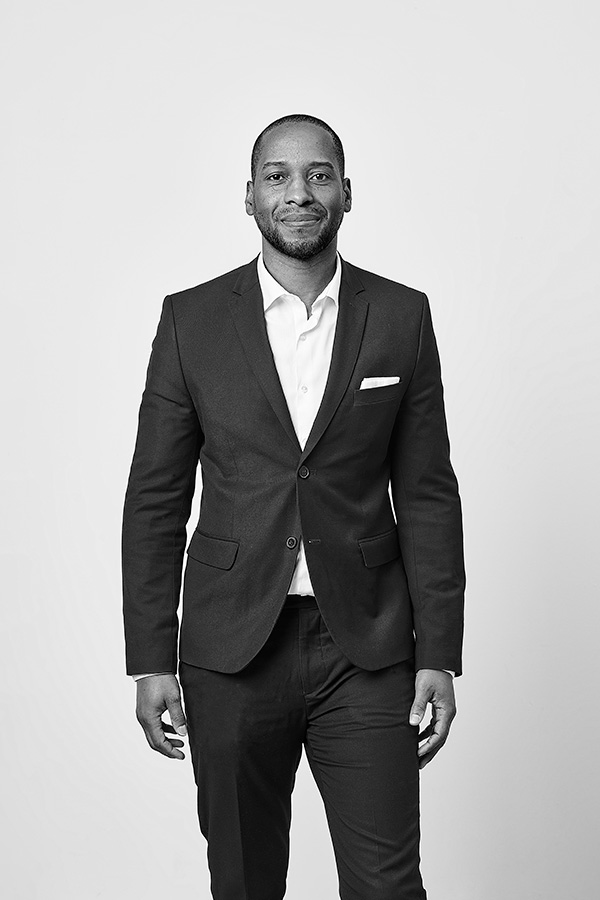 andre stands against a white background wearing a grey suit and white dress shirt.